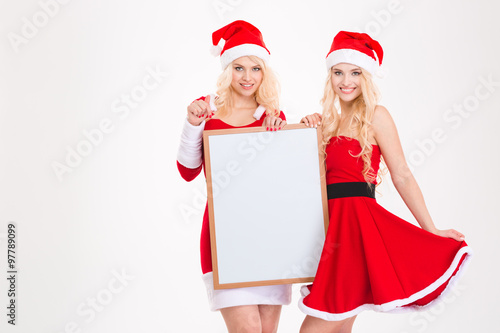 Two sisters in santa claus costumes posing with blank board