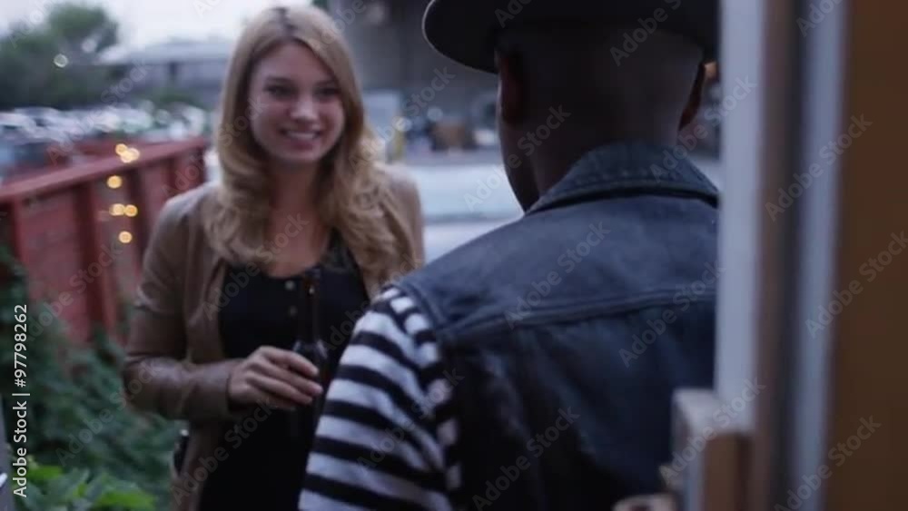 Over the shoulder shot of cute young couple laughing smiling and talking in doorway at party with drinks in hand Over the shoulder shot of cute young couple laughing smiling and talking in doorway at party with drinks in hand