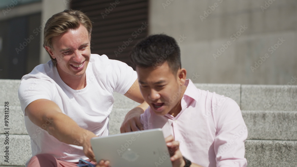 Casual male friends hanging out together in the city with a computer tablet Casual male friends hanging out together in the city with a computer tablet