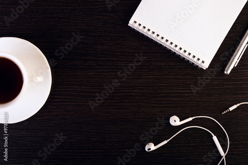 cup of hot coffee, headphones, notebook, pen on the wooden background. Place for text. Square image.