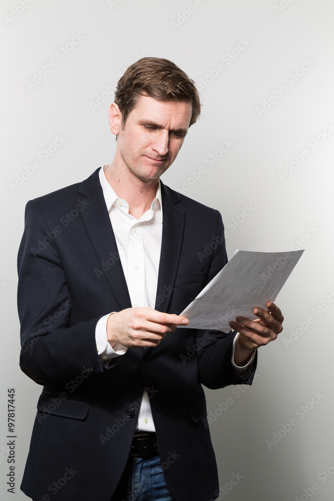 Blond-haired businessman takes a dubiously look at a piece of paper while in front of a gradient background Blond-haired businessman takes a dubiously look at a piece of paper while in front of a gradient background