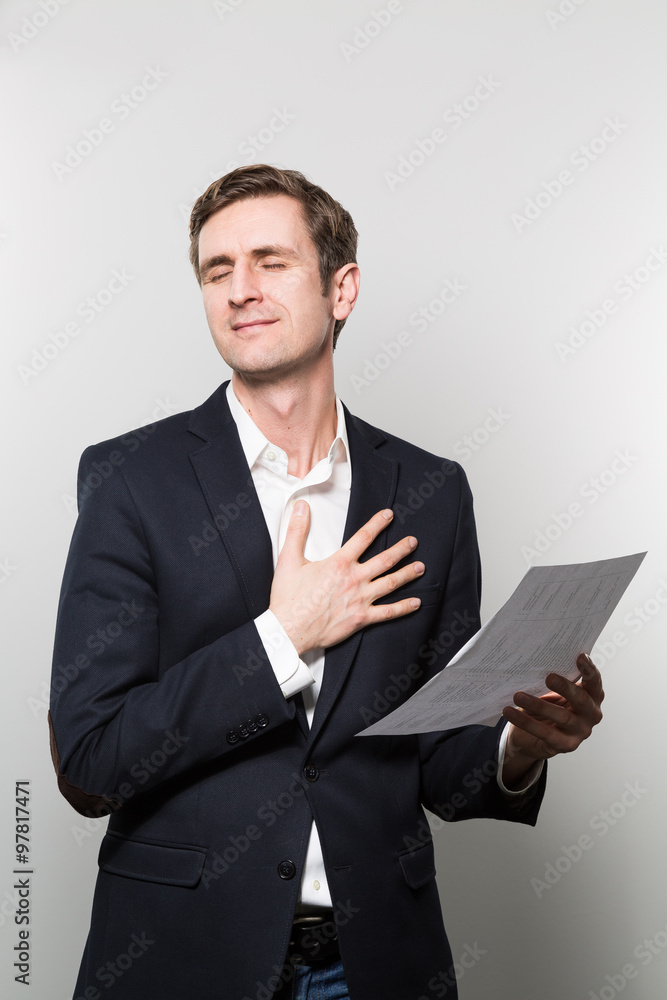 Blond-haired businessman puts his hand on his chest and feels a sigh of relief while in front of a gradient background Blond-haired businessman puts his hand on his chest and feels a sigh of relief while in front of a gradient background