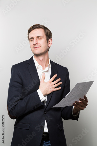 Blond-haired businessman puts his hand on his chest and feels a sigh of relief while in front of a gradient background