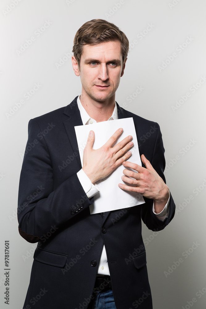 Blond-haired businessman presses a piece of paper to his chest with a serious look while in front of a gradient background Blond-haired businessman presses a piece of paper to his chest with a serious look while in front of a gradient background