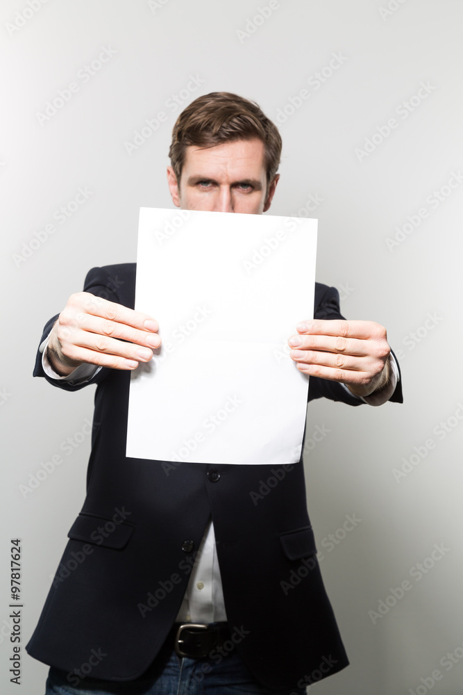 Blond-haired european businessman holds a piece of blank paper into the camera while in front of a gradient background Blond-haired european businessman holds a piece of blank paper into the camera while in front of a gradient background