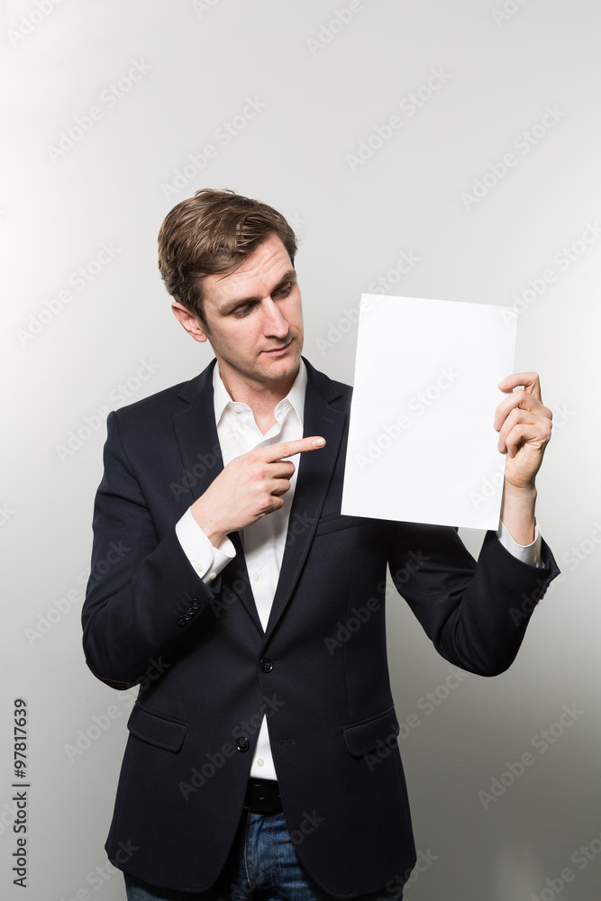 Blond-haired european businessman shows something on a piece of paper while in front of a gradient background Blond-haired european businessman shows something on a piece of paper while in front of a gradient background