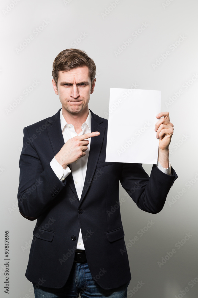 Blond-haired european businessman shows something on a piece of paper with squeezed eyes while in front of a gradient background Blond-haired european businessman shows something on a piece of paper with squeezed eyes while in front of a gradient background