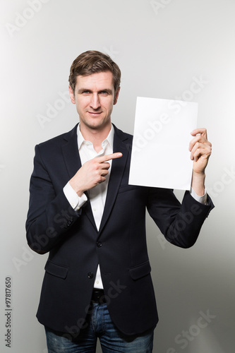 Blond-haired european businessman shows something on a piece of paper and takes a convincing glance into the camera while in front of a gradient background