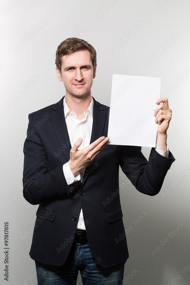 Blond-haired european businessman shows something on a piece of paper with a amiable face while in front of a gradient background Blond-haired european businessman shows something on a piece of paper with a amiable face while in front of a gradient background