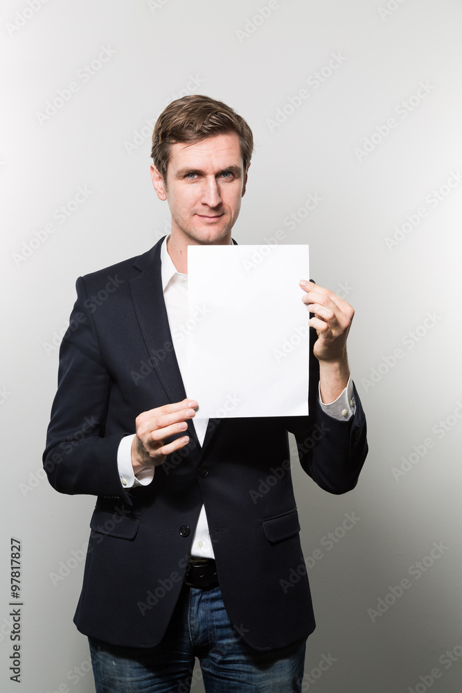 Blond-haired european businessman shows something on a piece of paper with a stern face while in front of a gradient background Blond-haired european businessman shows something on a piece of paper with a stern face while in front of a gradient background