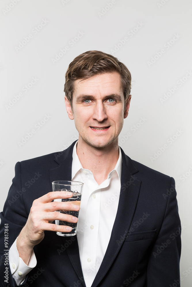 Blond-haired european businessman holding a glas of sparkling water with a satisfied look in front of a gradient background Blond-haired european businessman holding a glas of sparkling water with a satisfied look in front of a gradient background