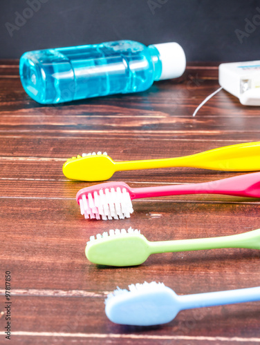 Set of colorful toothbrushs with mountwash and dental floss on wooden board