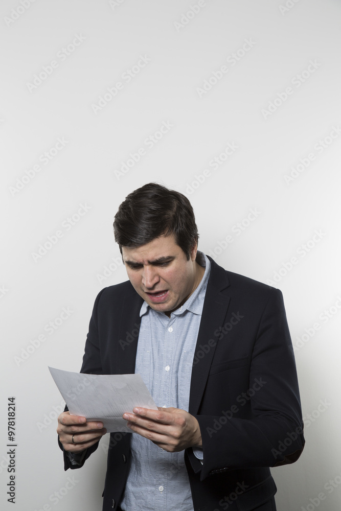 Dark-haired european businessman with a vine look stares at a piece of paper while in front of a gradient background Dark-haired european businessman with a vine look stares at a piece of paper while in front of a gradient background