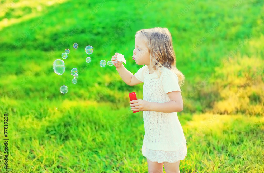 Happy little girl child blowing soap bubbles in summer day