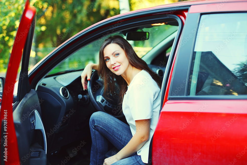 Beautiful smiling young woman driver behind the wheel red car