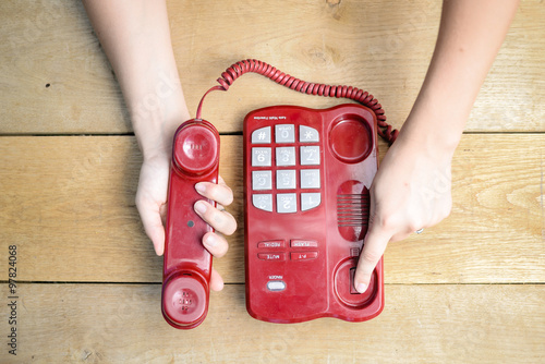 Closeup of female hands ending conversation by red cord telephone