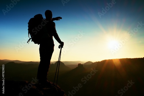 Sharp silhouette of a tall man on the top of the mountain with sun in the frame. Tourist guide in mountains photo