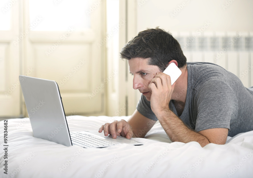 young attractive man lying on bed or couch using mobile phone and computer laptop working from home young attractive man lying on bed or couch using mobile phone and computer laptop working from home