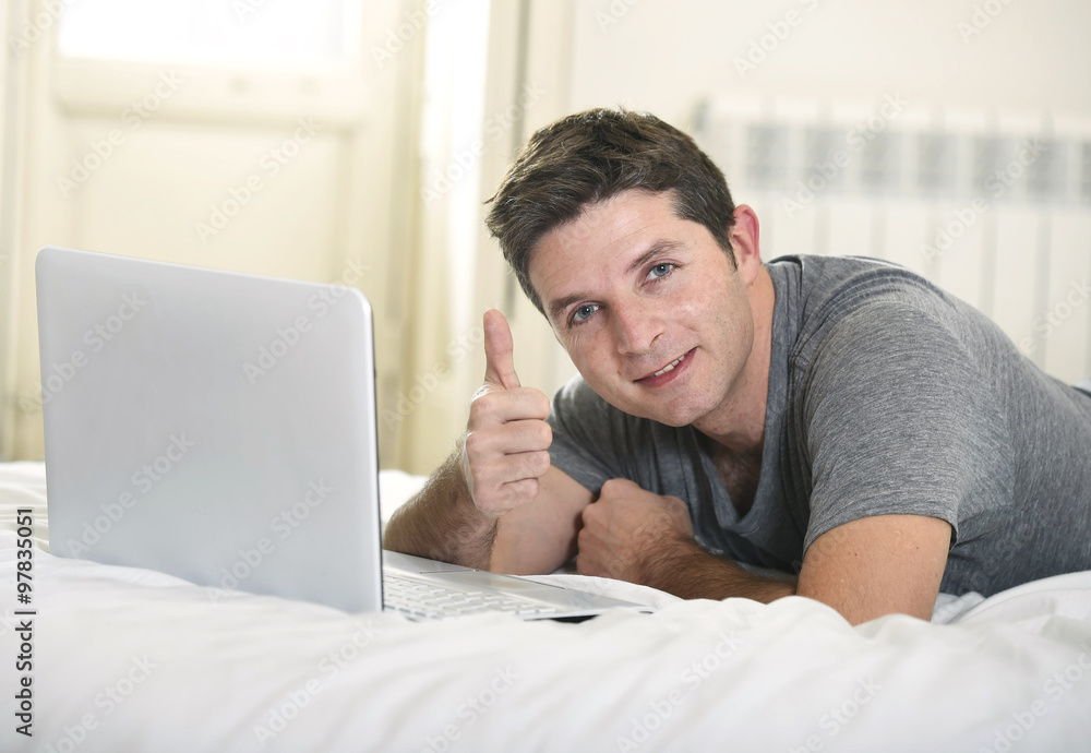 young attractive man lying on bed or couch enjoying social networking using computer laptop at home young attractive man lying on bed or couch enjoying social networking using computer laptop at home