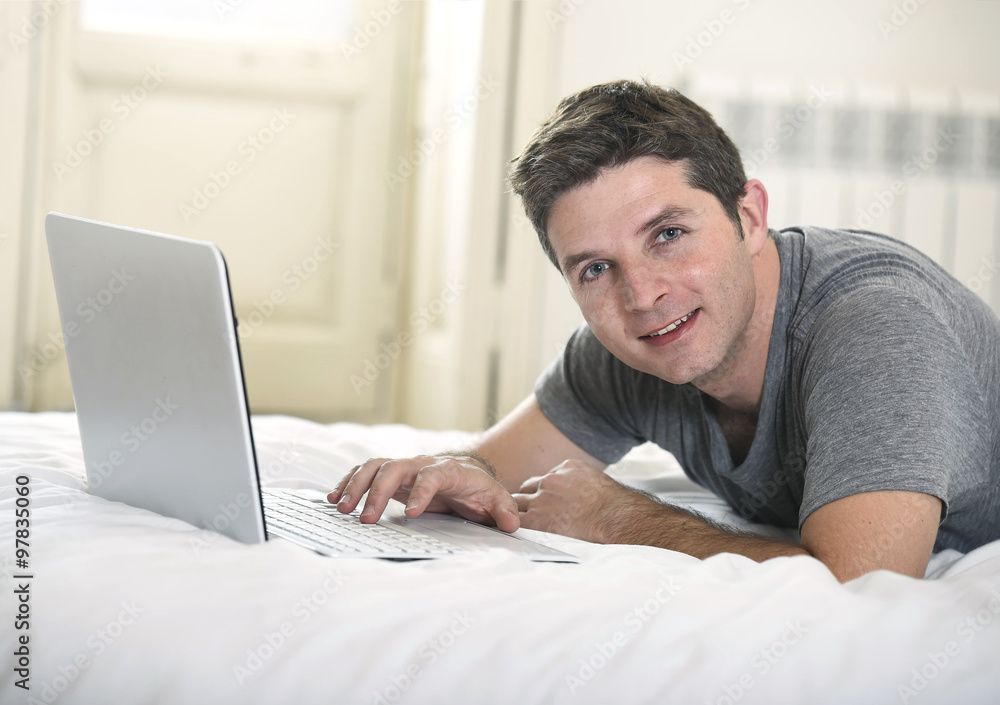 young attractive man lying on bed or couch enjoying social networking using computer laptop at home young attractive man lying on bed or couch enjoying social networking using computer laptop at home