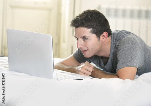 young attractive man lying on bed or couch enjoying social networking using computer laptop at home