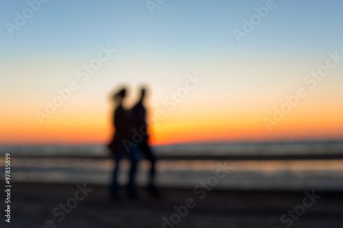 Two people defocused silhouettes walking along the beach on suns