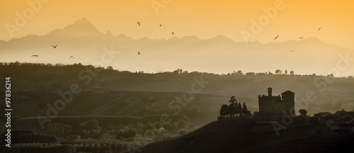 View the sunset over the hills of the Castle of Grinzane Cavour Unesco heritage in the territory of the Langhe Piedmont Italy, migratory birds flying in the sky