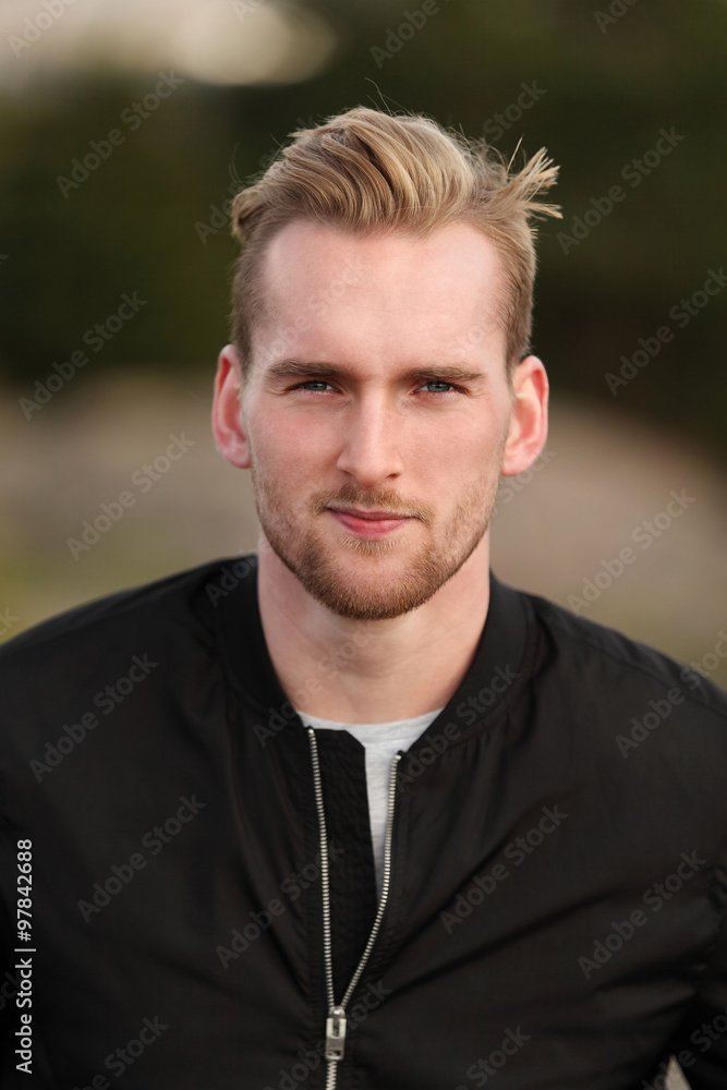 Handsome man wearing a black jacket and jeans sitting down outside on a bench on a cold windy autumn day. Handsome man wearing a black jacket and jeans sitting down outside on a bench on a cold windy autumn day.