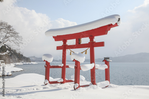 A red Torii gate of Japanese shrine and Lake Tazawa in snow