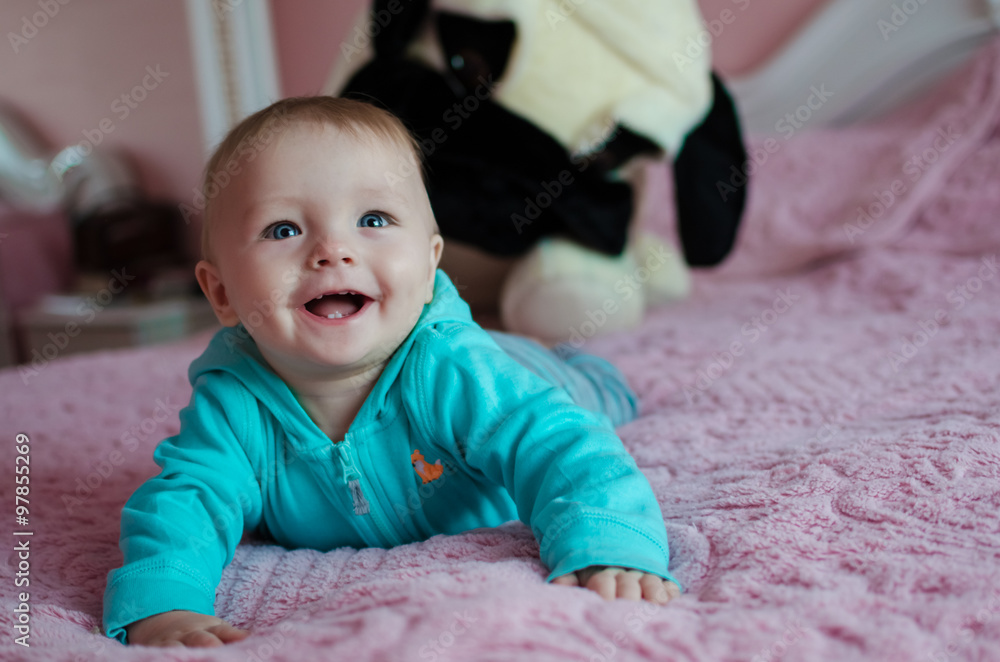 Cute smiling baby lying on tummy in parent's bed with a big toy dog on background. Happy baby. Cute smiling baby lying on tummy in parent's bed with a big toy dog on background. Happy baby.