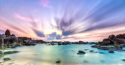 Dance of cloudy dawn on coastal reefs when long exposure makes clouds spun as theatrical streak in the sky  bottom reefs are interspersed waves undulating smooth real welcome new day beautiful