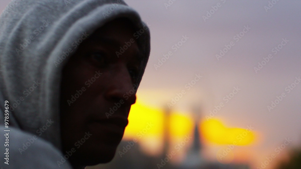 Athletic hooded man looks out over view of the city at sunset Athletic hooded man looks out over view of the city at sunset