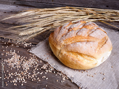 Homemade bread and ripe ears of wheat on a wooden background