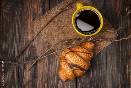 Coffee and croissant for breakfast on rustic wooden table, top view