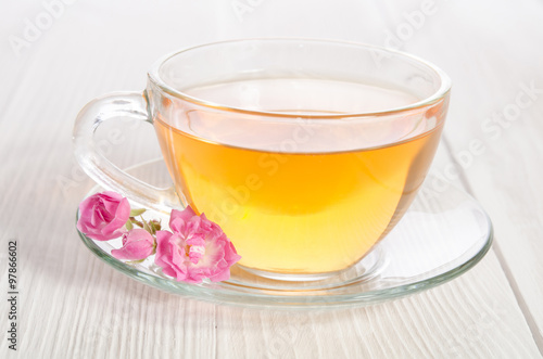 Glass cup of tea with rose on white wooden table