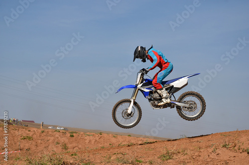 Fototapeta Naklejka Na Ścianę i Meble -  Motorcycle racer completes a jump, standing on a motorcycle motocross tilted forward