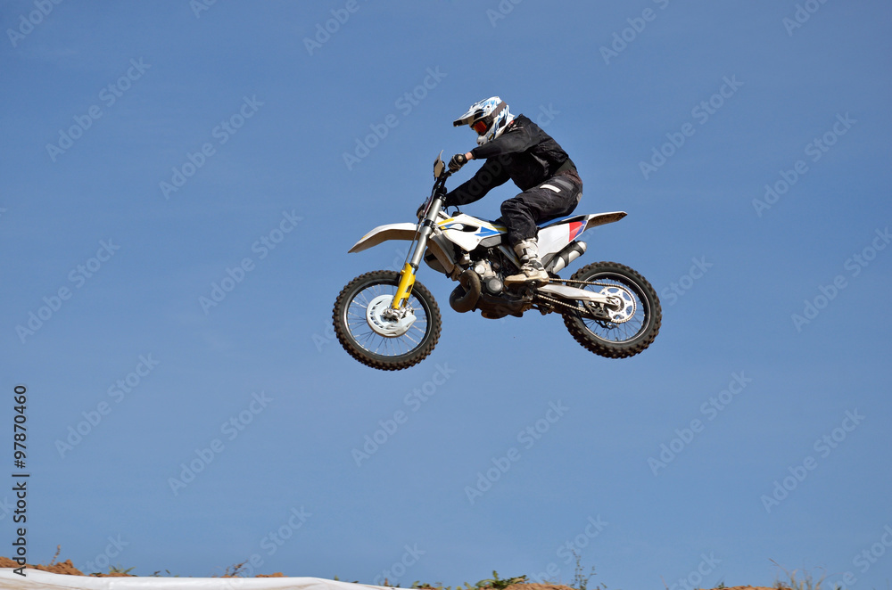 Tall flight on a white motorcycle athlete in a black clothes, against the clear blue sky Tall flight on a white motorcycle athlete in a black clothes, against the clear blue sky