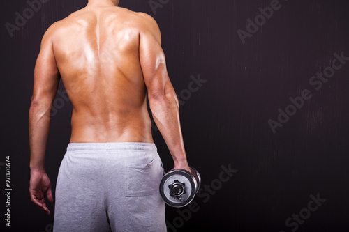 Back view of fit man holding a dumbbell on grunge background