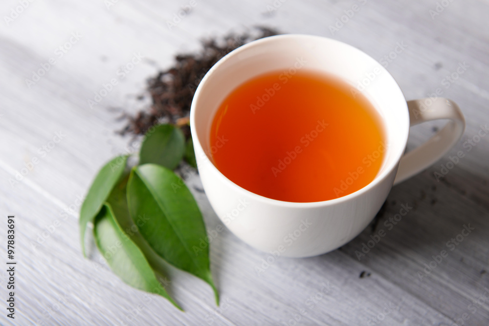 Ceramic cup of tea with scattered tea leaves around on light wooden background Ceramic cup of tea with scattered tea leaves around on light wooden background