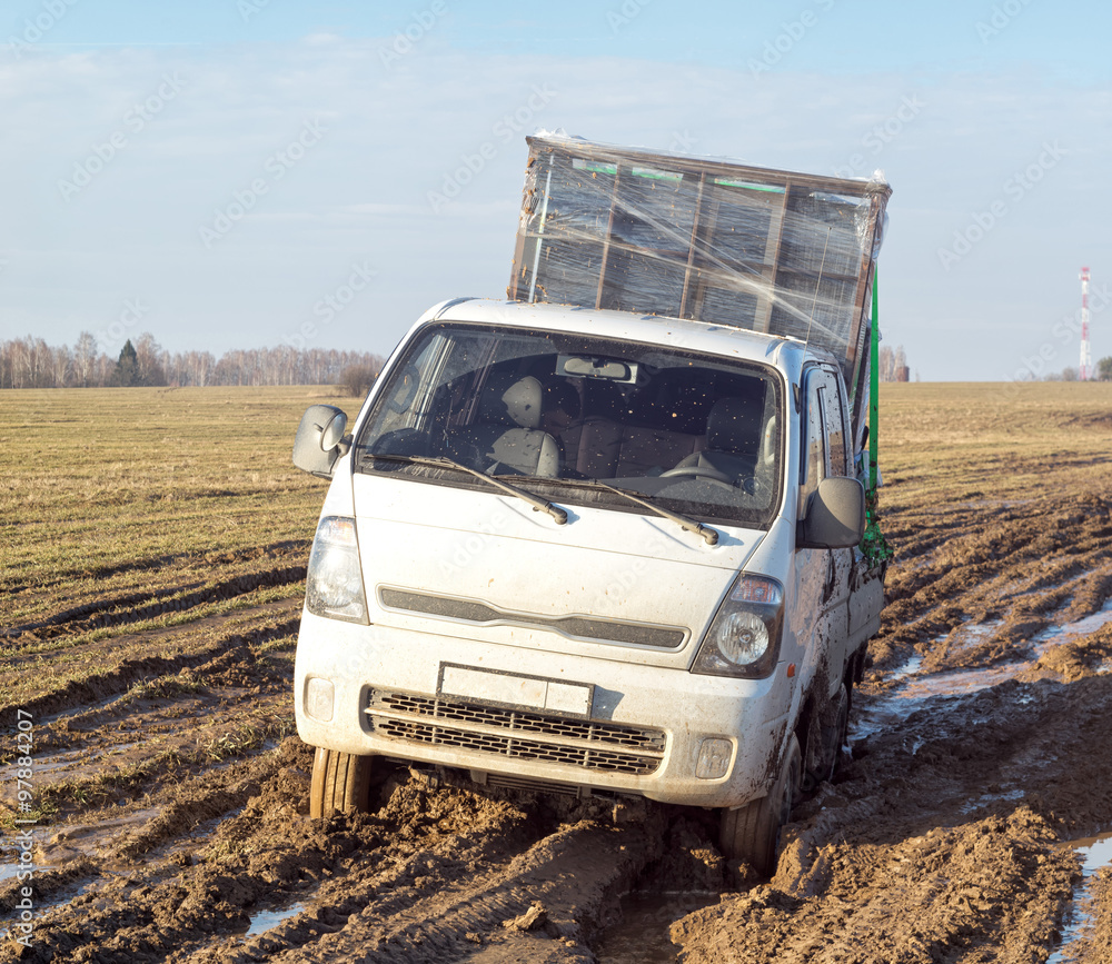 Off-road truck with furniture settles down in mud on dirty road in fallow field