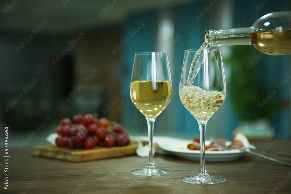 Pouring white wine from bottle into the wineglass on the table over blurred background Pouring white wine from bottle into the wineglass on the table over blurred background