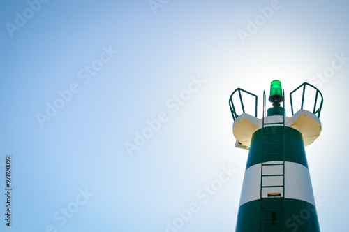 Lighthouse with green lantern on top on cloudless sky background