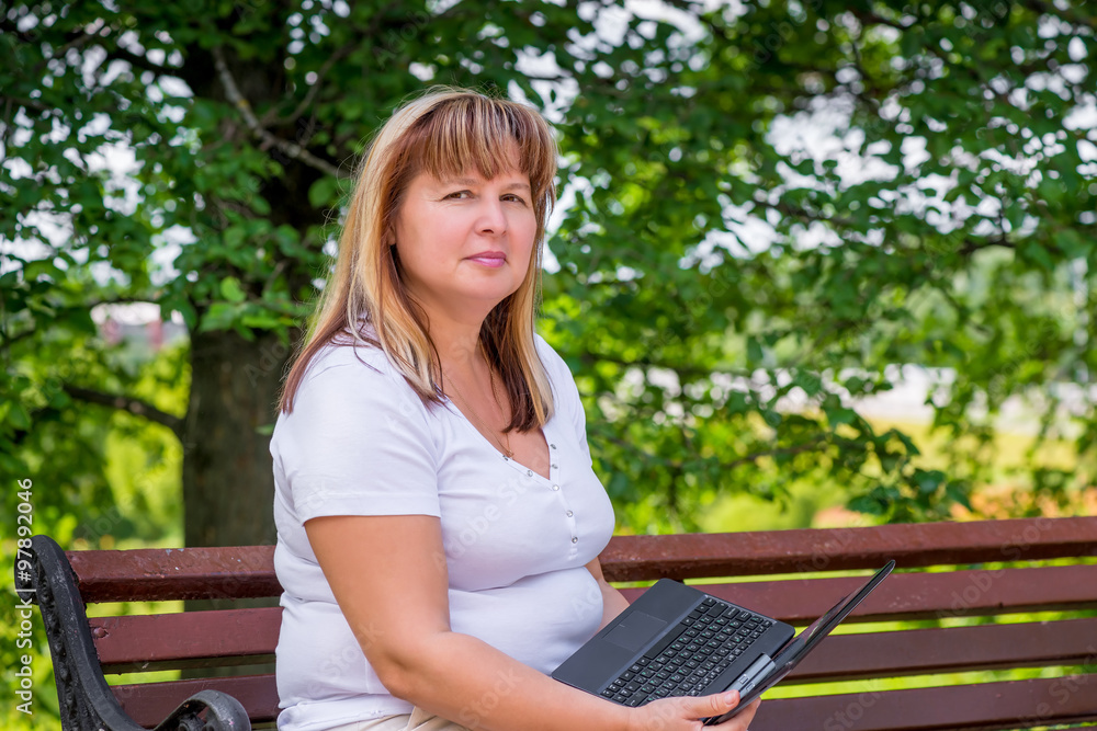 beautiful mature woman on a park bench with a laptop beautiful mature woman on a park bench with a laptop