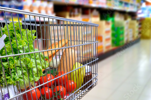 Obraz na plátne Shopping cart full of food in supermarket aisle side tilt