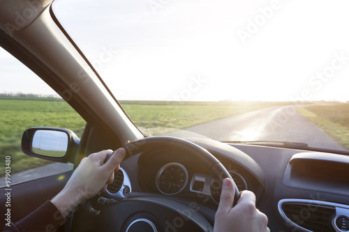 Hands of young driver on steering wheel during road trip with re