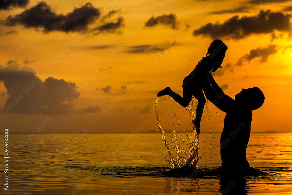 Father and litlle daughter in the sea at sunset on a tropical island