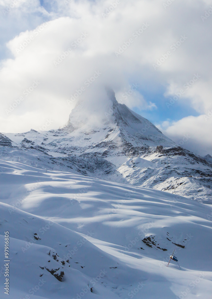 Amazing view on Matterhorn - famous mountain in Swiss Alps, with aerial view on Zermatt Valley, Switzerland, in a sunny winter day, with blue sky, clouds and view on ski resort
