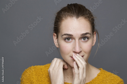 glowing happiness concept - confused 20s girl thinking with shy hand gesture for discretion and shyness,studio shot on gray background photo