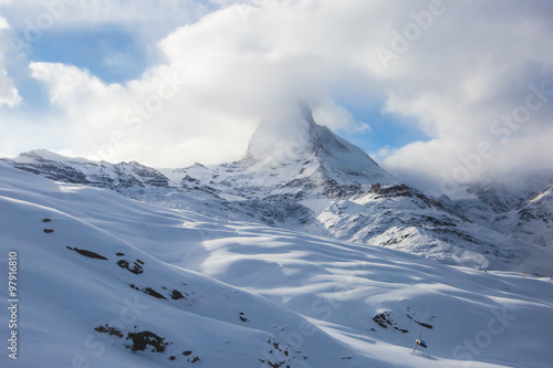 Amazing view on Matterhorn - famous mountain in Swiss Alps, with aerial view on Zermatt Valley, Switzerland, in a sunny winter day, with blue sky, clouds and view on ski resort 