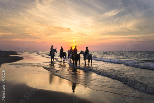 Jeźdźcy na koniach jadący brzegiem morza o zachodzie słońca 